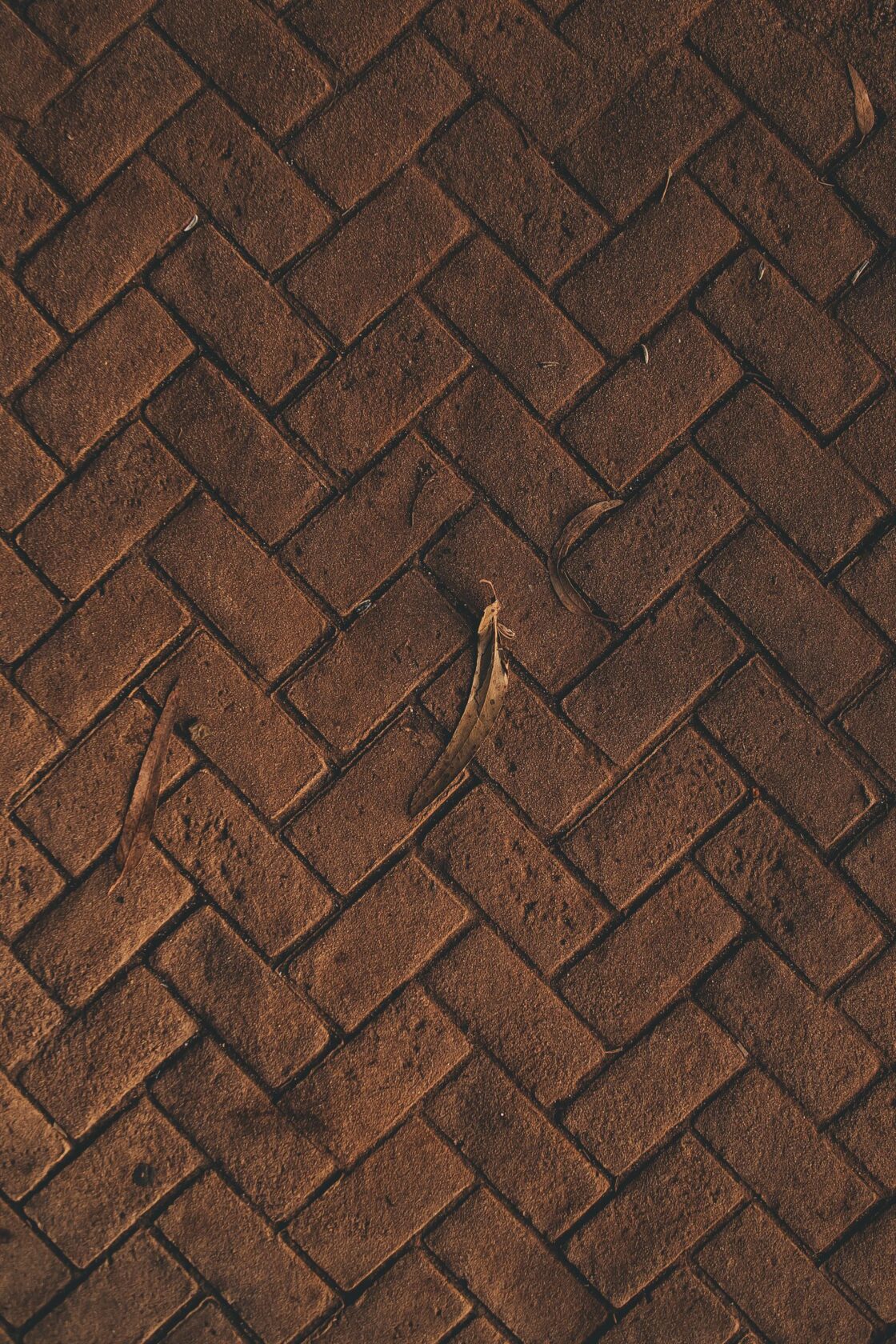 Close-up of a rustic brown herringbone brick pattern with rough texture and organic elements.
